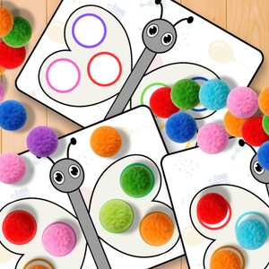 May include: Educational butterfly-themed game with colorful pom-poms. The game features butterfly-shaped cards with colored circles, designed for matching pom-poms by color. The pom-poms are in various colors, including orange, red, green, blue, and pink.