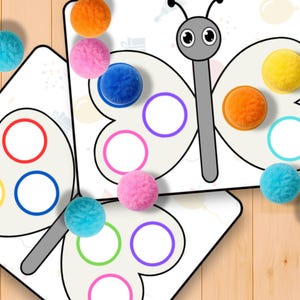 May include: Butterfly-shaped educational game with colorful pom-poms. The game features a white background with a gray butterfly outline and colored circles. The pom-poms are in various colors, including orange, pink, blue, and yellow. The game is designed for educational purposes.