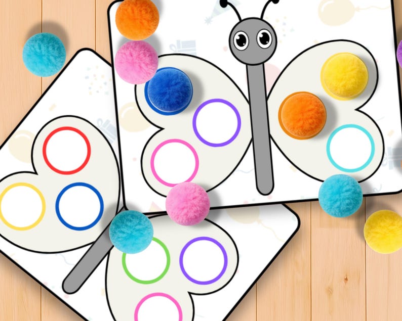 May include: Butterfly-shaped educational game with colorful pom-poms. The game features a white background with a gray butterfly outline and colored circles. The pom-poms are in various colors, including orange, pink, blue, and yellow. The game is designed for educational purposes.