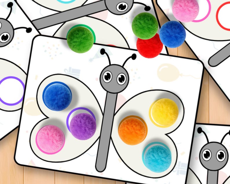 May include: Butterfly-shaped educational game with colorful pom-poms. The game features a white background with a butterfly outline and matching colored circles. Various colored pom-poms are scattered around the game, including green, red, blue, and pink.