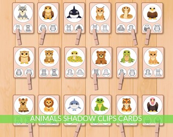 Puede incluir: Tarjetas de clip de sombra de animales con ilustraciones de animales como un lobo, un búho y una serpiente. Cada tarjeta tiene siluetas de sombra coincidentes debajo. Las tarjetas se sujetan con pinzas de madera. El texto "ANIMALS SHADOW CLIPS CARDS" está en la parte inferior.