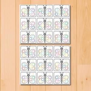 May include: Two sets of butterfly-themed flashcards. Each card features a gray butterfly with colorful circles on its wings. The cards are arranged in a grid pattern on a light wooden surface.