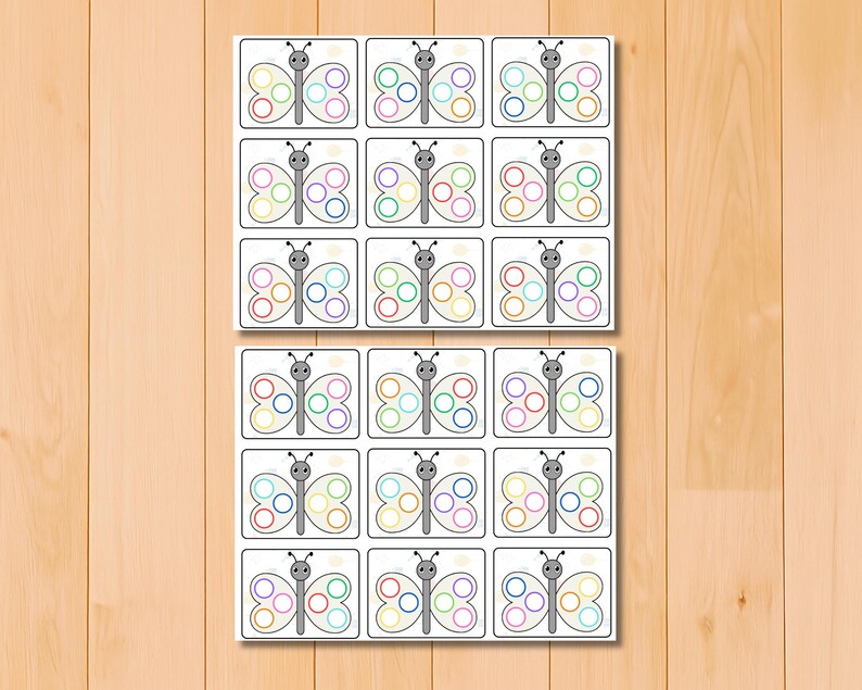 May include: Two sets of butterfly-themed flashcards. Each card features a gray butterfly with colorful circles on its wings. The cards are arranged in a grid pattern on a light wooden surface.