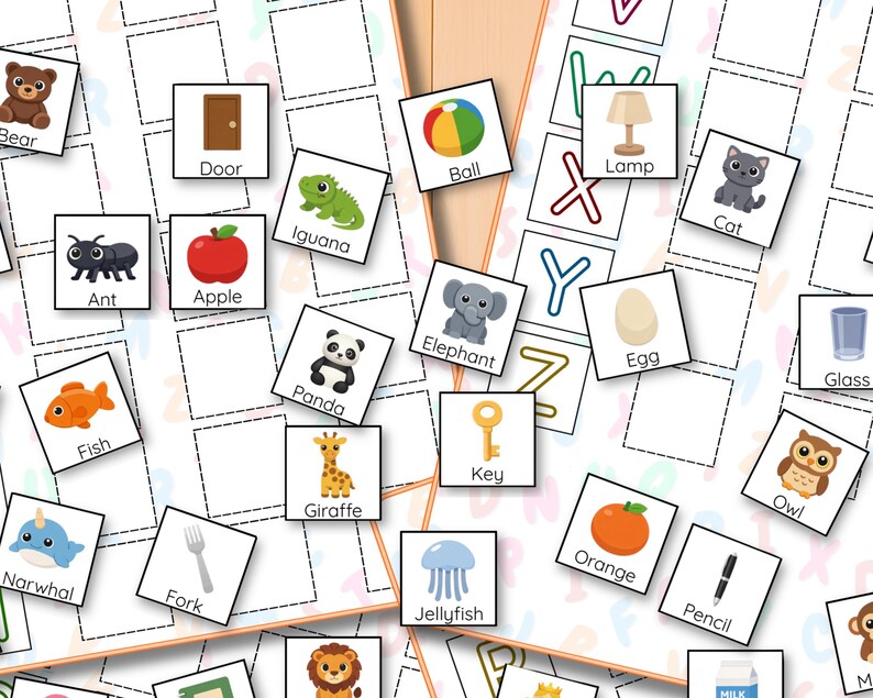 May include: Flashcards with illustrations of objects and animals, including a bear, apple, and panda. Each card has a corresponding word, such as "Ball" and "Egg", designed for educational purposes. The cards are arranged on a white surface.