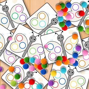 May include: A collection of white butterfly-shaped cards with colorful circles and gray stems, scattered with colorful pom-poms. The cards feature a cartoon butterfly design with three colored circles on each wing. The pom-poms are in various colors.