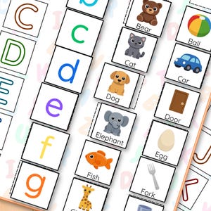 May include: Alphabet flashcards for education, featuring colourful letters and corresponding illustrations. Includes images of a bear, cat, dog, elephant, and fish. The cards are arranged on a light-coloured surface.