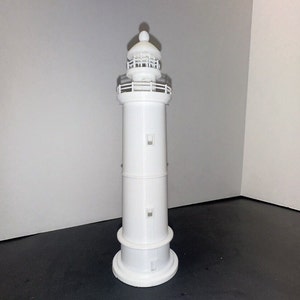 May include: A white plastic model of a lighthouse with a small, round top and a railing around the top of the tower. The lighthouse has two small windows on each side of the tower.