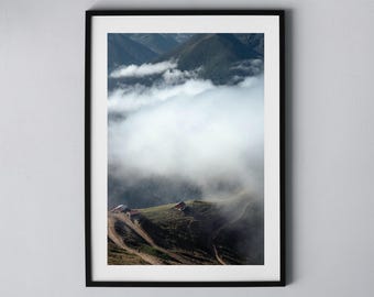 May include: A photograph of a mountain range with a thick layer of fog covering the peaks. Two small buildings are visible on the side of the mountain.