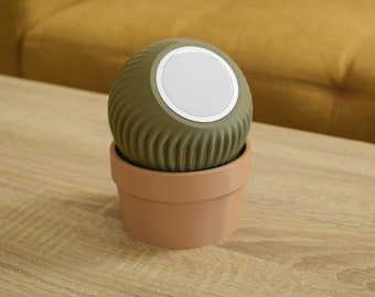 May include: A green, round speaker with a white speaker grille sits in a terracotta pot on a wooden table.