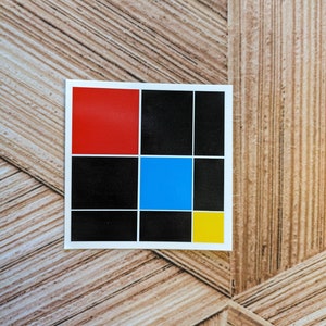 May include: A sticker with a grid of nine squares. The top left square is red, the top middle square is black, the top right square is black, the middle left square is black, the middle center square is blue, the middle right square is black, the bottom left square is black, the bottom middle square is black, and the bottom right square is yellow.