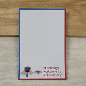 May include: A white card with a blue and red border. The card features a wooden toy with colorful blocks and the text "It is through work alone that a child develops."