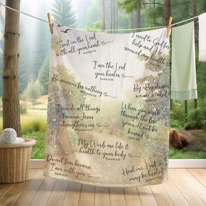 May include: A watercolor-style throw blanket with inspirational Bible verses and quotes printed on it. The background is a soft green and brown with a watercolor effect. The text is in black and white.