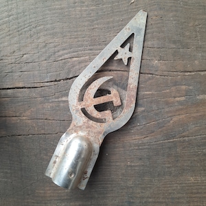 Puede incluir: Un adorno para árbol de Navidad de metal, oxidado y deslustrado, decorativo, ornamental o vintage en forma de estrella con un martillo y una hoz en su interior.