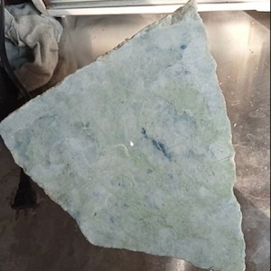 May include: A large, irregularly shaped piece of light green jade with white and dark green veins. The jade is smooth and polished.