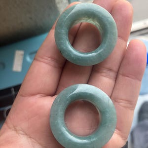 Puede incluir: Dos expansores de oreja circulares de color verde jade. Los expansores son lisos y tienen un aspecto translúcido. El color es un verde suave y apagado. Los expansores se muestran sobre un fondo neutro.