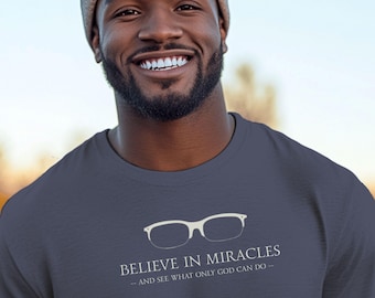 May include: A navy blue t-shirt with the text "BELIEVE IN MIRACLES - AND SEE WHAT ONLY GOD CAN DO -" and a white glasses graphic. The person in the image is wearing a grey beanie.