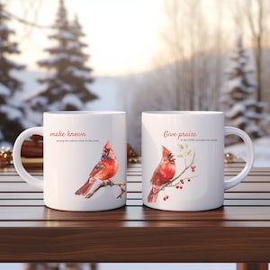 May include: Two white ceramic mugs with a red cardinal bird design. The mug on the left says "make known among the nations what he has done." The mug on the right says "Give praise to the LORD proclaim his name."