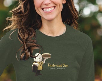 May include: Dark green long-sleeve shirt with a graphic of a cartoon character holding a sandwich. The text "Taste and See that the Lord is good!" is printed on the shirt. The shirt is made of a soft material.