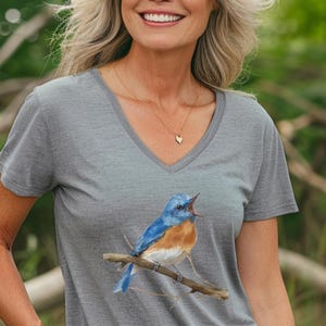 May include: A heather grey V-neck t-shirt with a watercolor illustration of a bluebird singing on a branch.