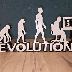 Könnte beinhalten: Schwarz-weiße Holzskulptur, die die menschliche Evolution vom Affen bis zu einer Person am Computer darstellt. Das Wort "EVOLUTION" steht am Sockel. Die Skulptur steht auf einer Holzoberfläche.