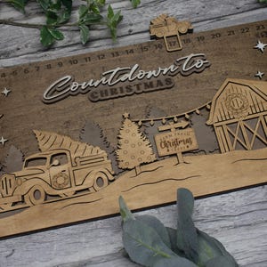 May include: Wooden countdown calendar with a Christmas theme. The calendar features a red truck with a Christmas tree in the back, a barn, and a sign that says "Farm Fresh Christmas Trees". The numbers 1 through 24 are displayed on the calendar.