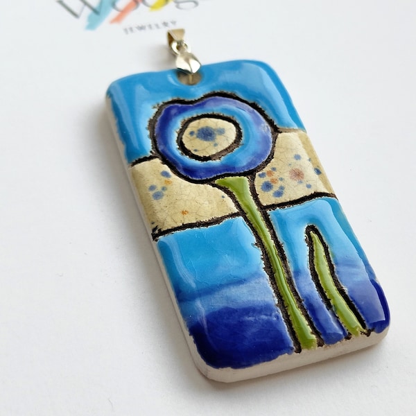 Blue flower on the beach background with amber, rectangular pendant with a plant motif, ceramic jewelry, inspired by the sea, summer atmosphere