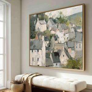 May include: An abstract painting of a village with white buildings and gray rooftops, set against a green hillside. The artwork is framed in a light wood and hangs above a white bench with a beige throw and a decorative pot.