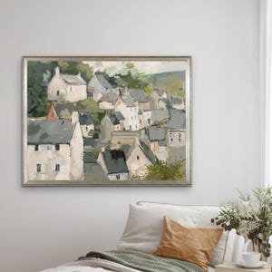 May include: A framed landscape painting depicts a village nestled in a valley. The artwork features white buildings with gray rooftops, surrounded by green foliage. The painting has a muted color palette and a textured appearance.