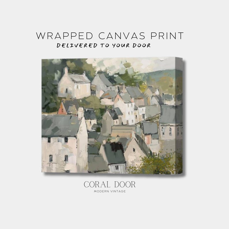 May include: Wrapped canvas print of a village scene. The artwork depicts a cluster of buildings with white walls and gray roofs, set against a backdrop of green hills. The text "Delivered to your door" is above the image. The text "Coral Door Modern Vintage" is below the image.