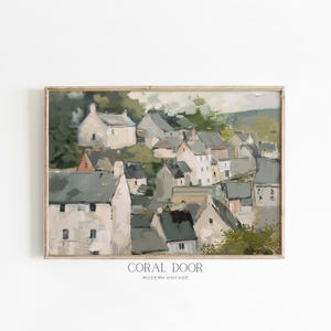May include: A framed landscape painting depicts a village nestled on a hillside. The artwork features muted tones of gray, white, and green, with visible brushstrokes. The text "CORAL DOOR MODERN VINTAGE" is at the bottom.