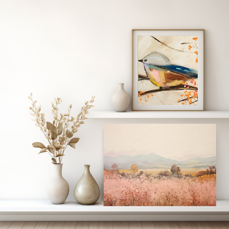 以下が含まれることがあります： 白い棚に、額縁に入った絵画が2枚と花瓶が3つ置かれています。左の絵画には、オレンジ色の葉のついた枝に青い鳥が描かれています。右の絵画には、ピンク色の野原と背景に山脈のある風景が描かれています。