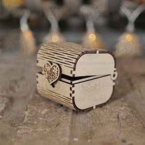 May include: A small, open wooden chest with a heart-shaped clasp. The chest is made of light-colored wood with a curved top and a decorative heart on the front. The chest is designed with a laser-cut pattern.