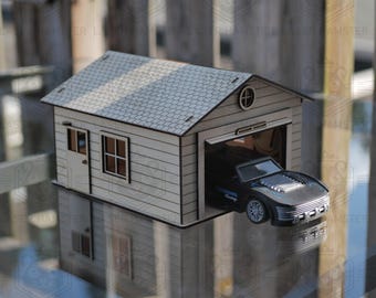 May include: A miniature wooden garage with a gray shingled roof and a small round window. A black toy car is parked inside the open garage. The garage has a white door and a window.