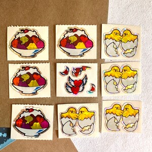 May include: Nine vintage stickers featuring a colorful ice cream sundae and two yellow chicks in eggshells. The stickers are on a brown background.
