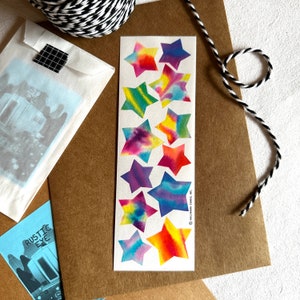 May include: A sheet of colorful tie-dye star stickers. The stars are arranged vertically in a row. The stars are in shades of blue, purple, green, orange, yellow, and red.
