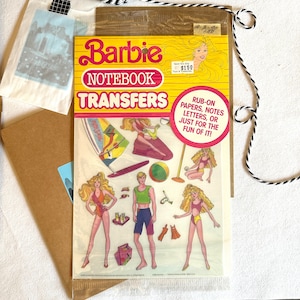 May include: A vintage Barbie Notebook Transfers sheet with a colorful design featuring a girl in a swimsuit on a surfboard, a girl in a swimsuit on a beach chair, a boy in a swimsuit, and a girl in a swimsuit with a beach bag. The sheet includes rub-on papers, notes, letters, or just for the fun of it! The text on the sheet reads "Barbie Notebook Transfers" and "Rub-on Papers, Notes Letters, or Just for the Fun of It!"