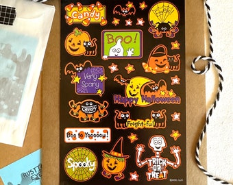 May include: A sheet of black Halloween stickers with various designs, including pumpkins, ghosts, bats, spiders, candy corn, and a skeleton. The stickers feature phrases like "Candy", "Boo!" and "Happy Halloween".