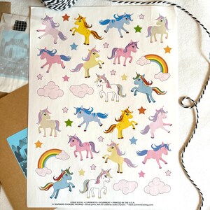May include: A sheet of colorful unicorn stickers with a rainbow, clouds, and stars. The unicorns are in various colors, including pink, blue, yellow, and purple.