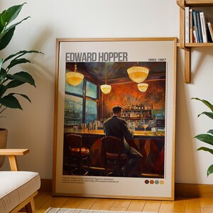 May include: A framed print of a painting by Edward Hopper, titled "Nighthawks". The painting depicts a diner at night with three customers and a lone waiter. The diner is brightly lit, while the street outside is dark. The painting is set against a light brown background with a white border.