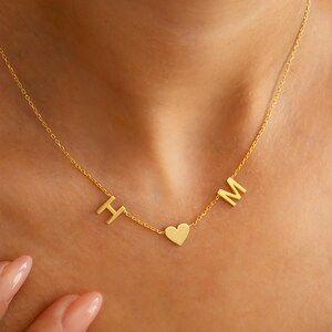 May include: A gold chain necklace with a heart charm and letter charms that spell "H M".