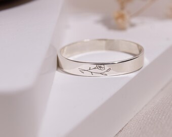 May include: A silver ring with a delicate floral design engraved on the band. The ring is on a white surface.