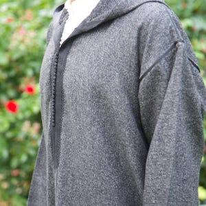 May include: A gray hooded robe with a zipper closure and black trim. The robe has a textured fabric and a relaxed fit.