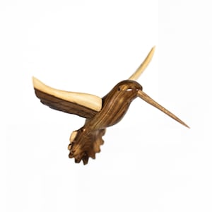 May include: A wooden hummingbird sculpture with brown and light wood tones. The sculpture is carved in detail and has a long beak.