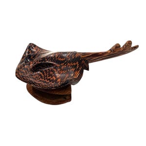 May include: A wooden sculpture of a stingray with a brown and black patterned body. The stingray is mounted on a wooden base.