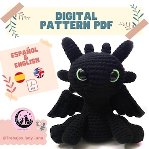 Puede incluir: Un dragón negro tejido a ganchillo con ojos verdes y pequeñas alas. La imagen incluye el texto "DIGITAL PATTERN PDF" y "ESPAÑOL & ENGLISH" con banderas y un icono PDF. El dragón está sentado sobre una superficie blanca.