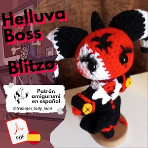 Puede incluir: Un juguete amigurumi de crochet rojo y negro de un personaje de la serie "Helluva Boss". El juguete está de pie sobre una base de madera. El texto "Patrón amigurumi en español" y "@trabajos_lady_luna" son visibles en la imagen. También se ve un icono de PDF y una bandera española.
