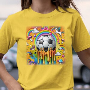 Könnte beinhalten: Ein gelbes T-Shirt mit einem Aufdruck eines Fußballs, der mit geschmolzenem Gold tropft. Der Aufdruck enthält auch Regenbögen, Wolken, Sterne, Süßigkeiten und ein Einhorn.