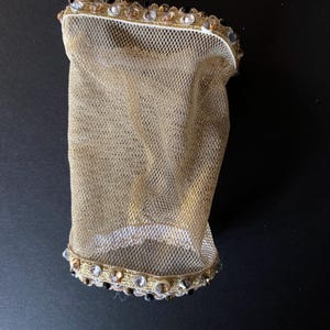 May include: A gold mesh fabric sleeve with a white and gold trim and black and clear rhinestones.