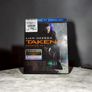 May include: A DVD of the movie "Taken" starring Liam Neeson. The cover features a seated man and the text "Taken Unrated Cut." The disc set includes an alternate ending and a black ops kill counter. The text "I'm going to do what I do best" is also visible.