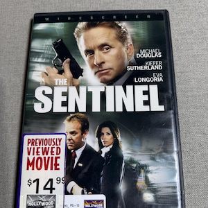 Puede incluir: DVD de la película "The Sentinel" con Michael Douglas, Kiefer Sutherland y Eva Longoria. La carátula presenta a los actores y el título de la película. Una pegatina indica que es una película previamente vista.